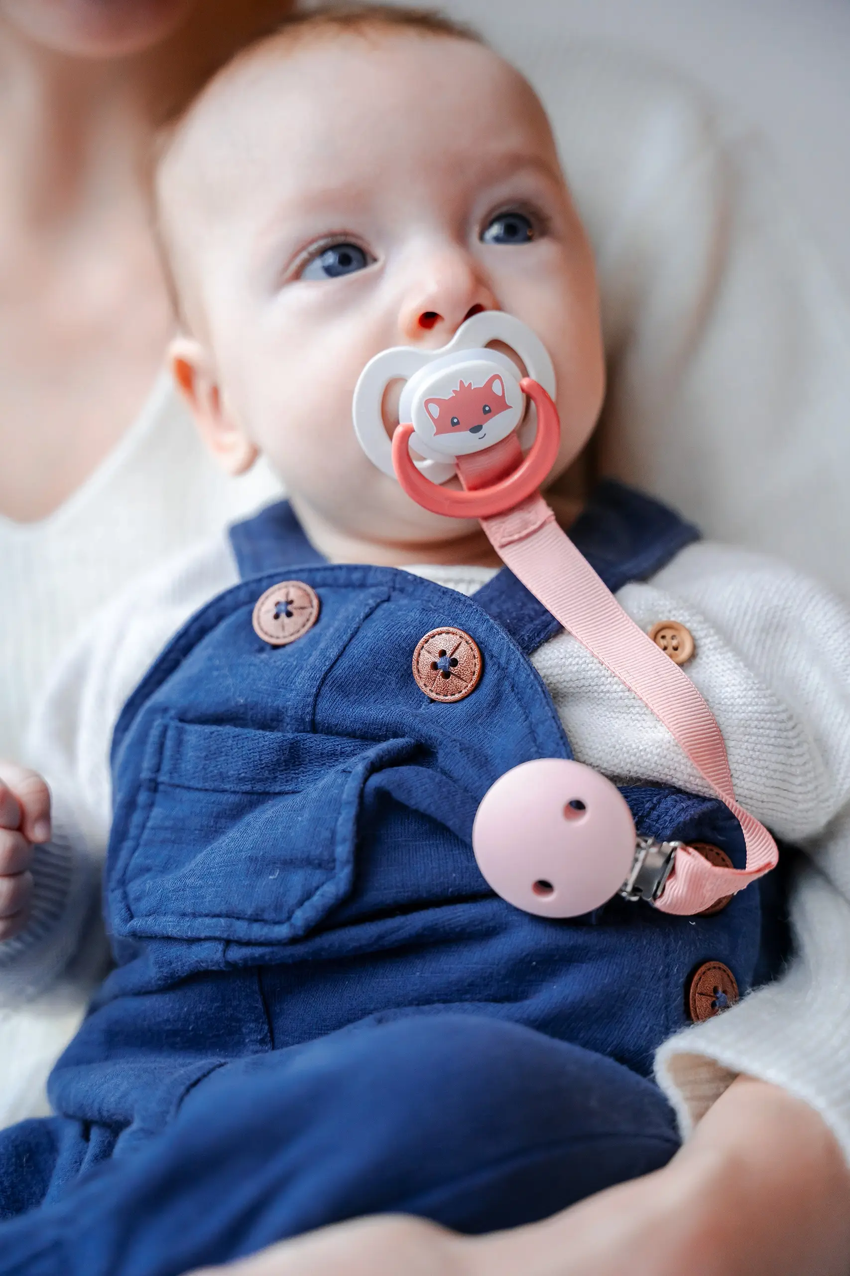 Baby in Jeans-Latzhose mit Schnuller im Mund